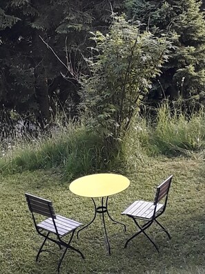 Relax in a serene outdoor setting with a round table and two comfortable chairs surrounded by lush greenery.
