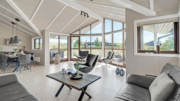 A spacious living area with a high ceiling, large windows offering a view of the outdoors, and modern furniture.