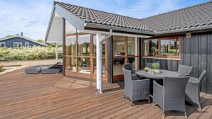 A modern house with a wooden deck, a glass-enclosed patio, and outdoor furniture.