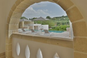 An outdoor pool area with lounge chairs and umbrellas, surrounded by a stone archway.