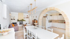 Une cuisine moderne avec des meubles blancs, un coin repas doté d’une table et de chaises blanches, et une arche en pierre.
