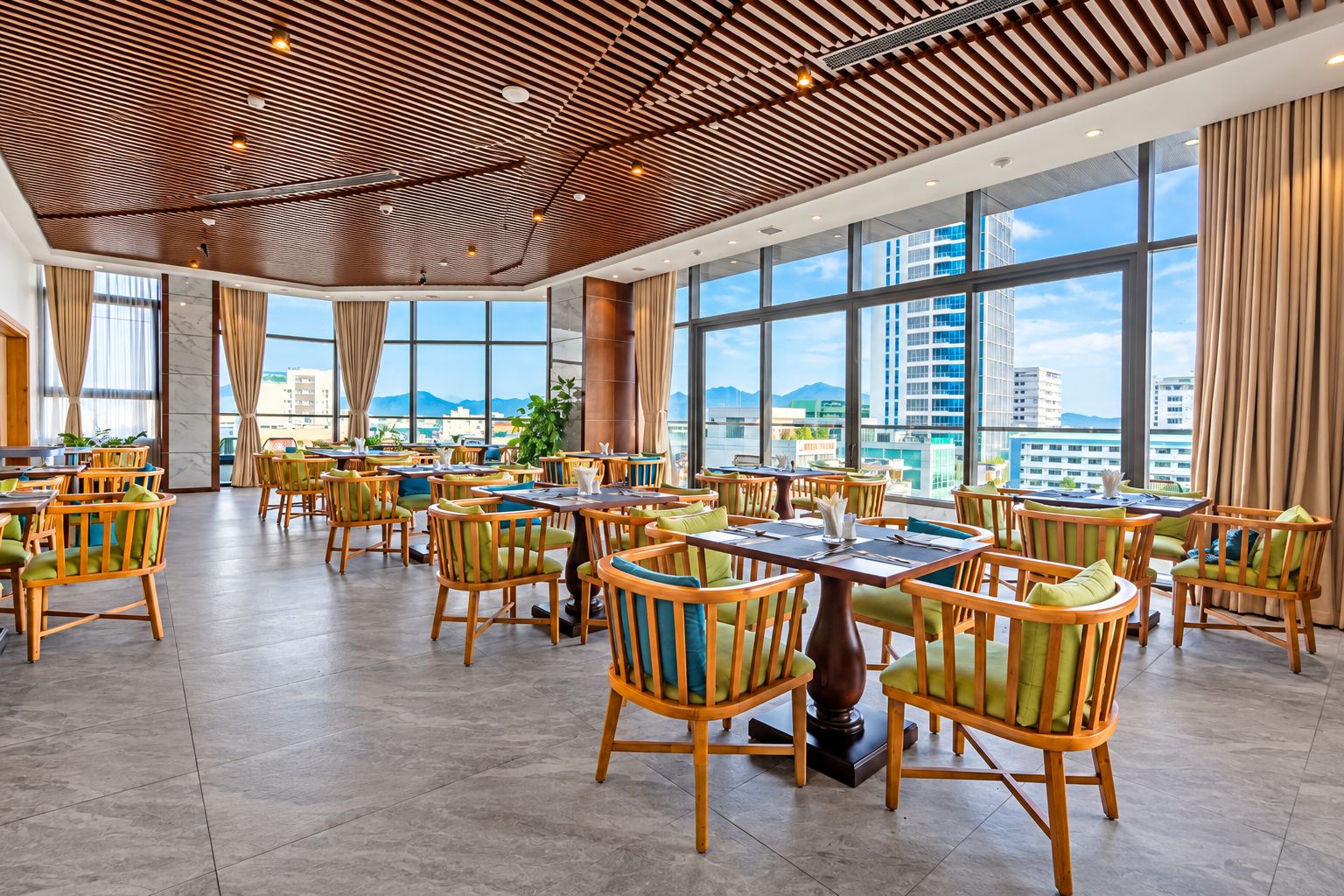 A spacious indoor area with multiple tables and chairs, large windows offering a view of the cityscape, and a ceiling with a wooden slatted design.