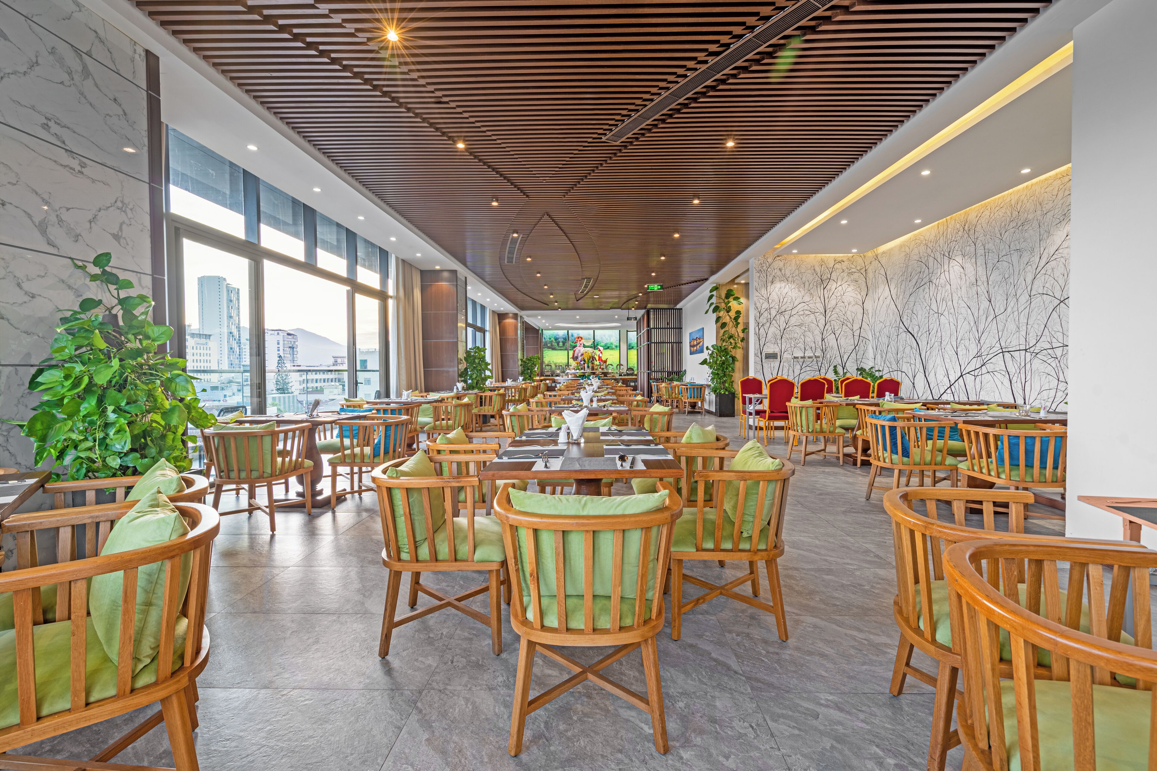 A spacious indoor dining area with wooden chairs and tables, large windows offering a city view, and a modern ceiling design.