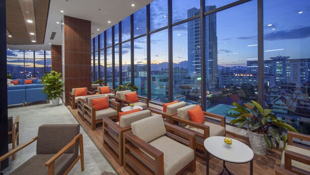A modern lounge area with sofas and chairs, large windows offering city views, and a pool visible through the windows.