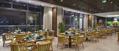 Un restaurante espacioso con sillas y mesas de madera, amplias ventanas que ofrecen vistas a la ciudad y un diseño de techo moderno.