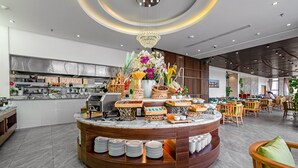 A modern restaurant with a central buffet area, a chandelier, and a seating area with wooden chairs and tables.
