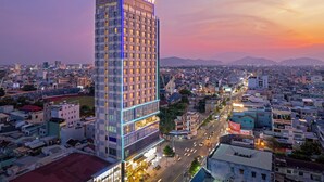 A high-rise hotel with a prominent 'Luxury' sign, surrounded by a cityscape with a sunset sky.