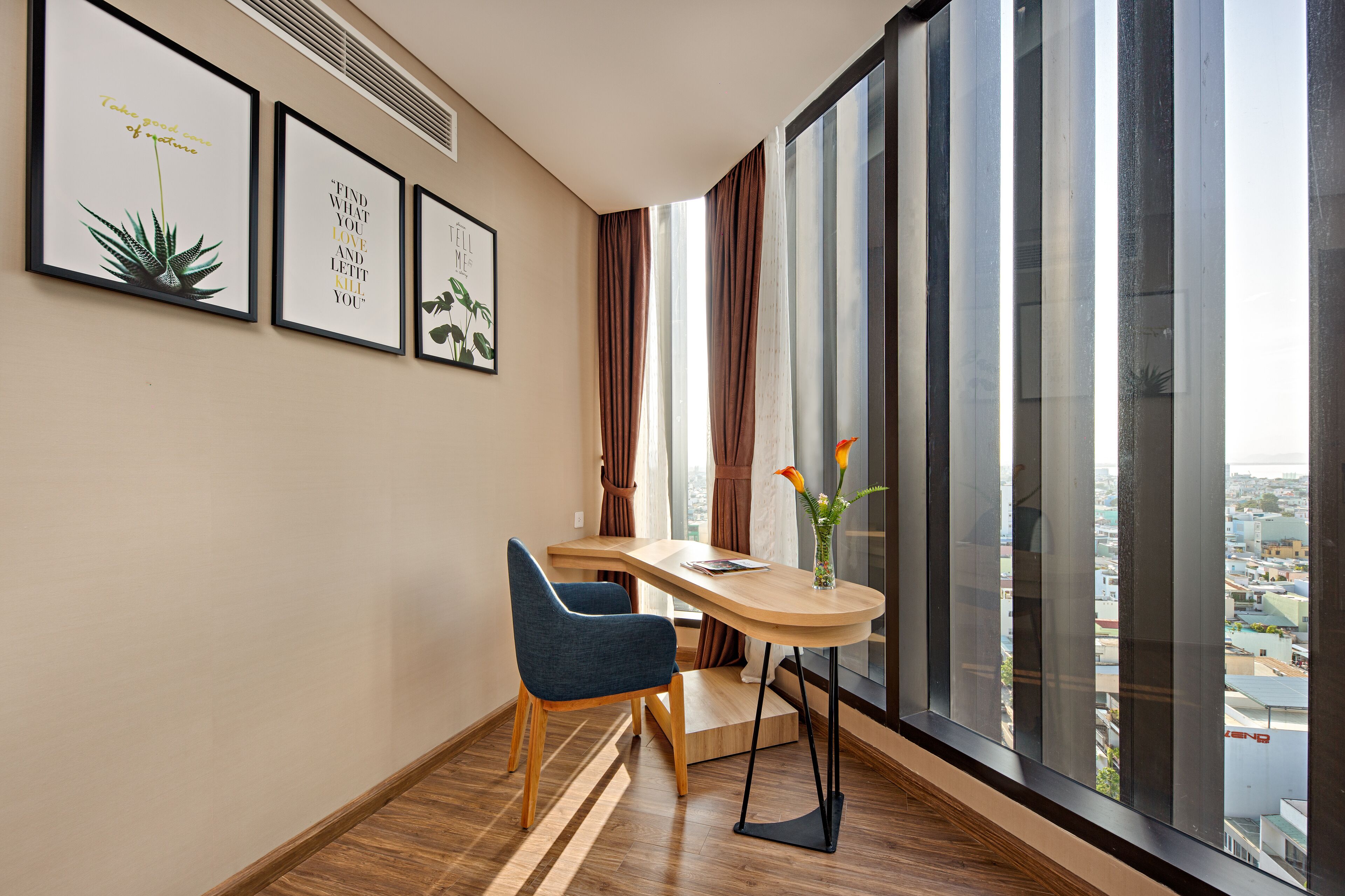 A modern room with a large window, a desk, a chair, and framed artwork on the wall.
