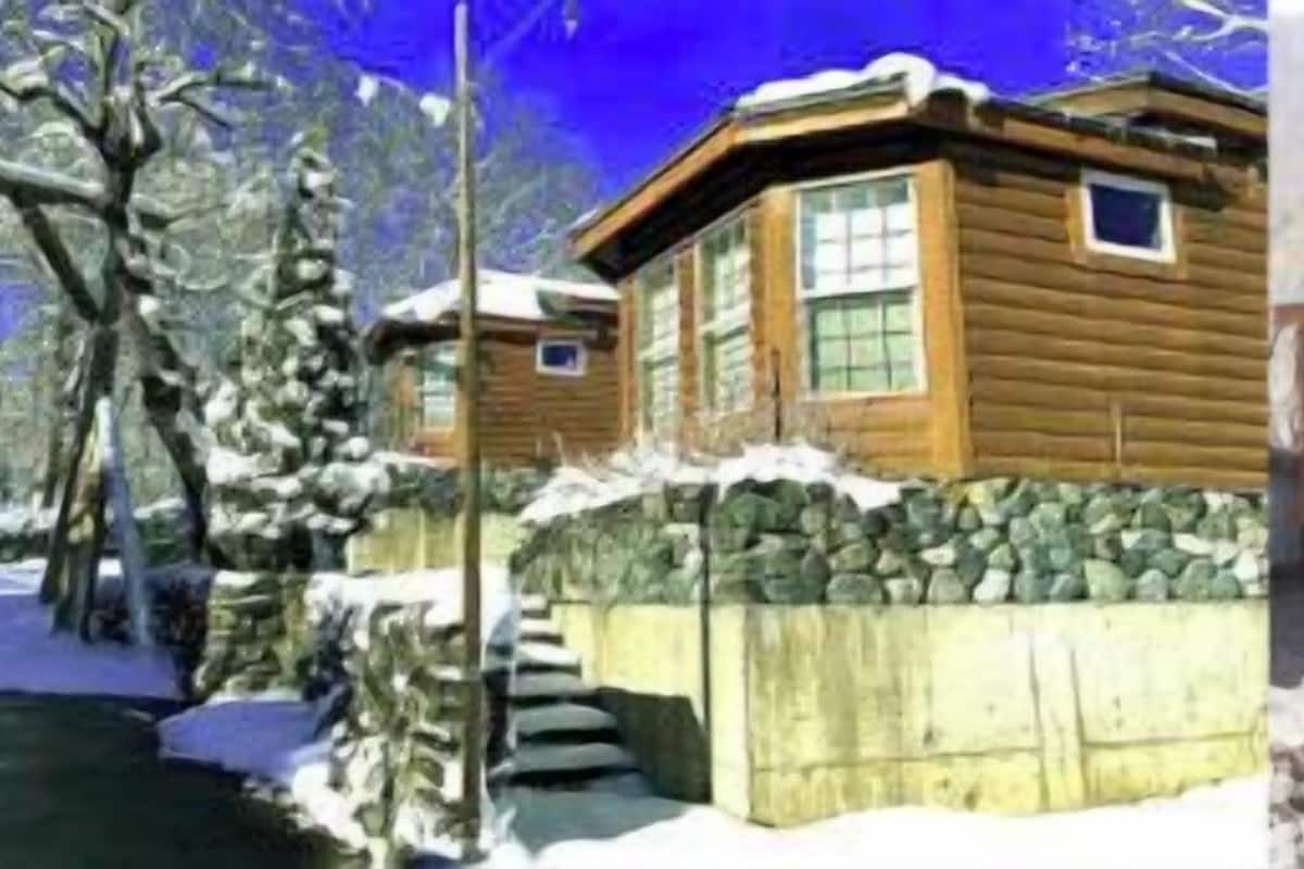 A wooden cabin with a stone foundation, a small porch, and a stone wall.