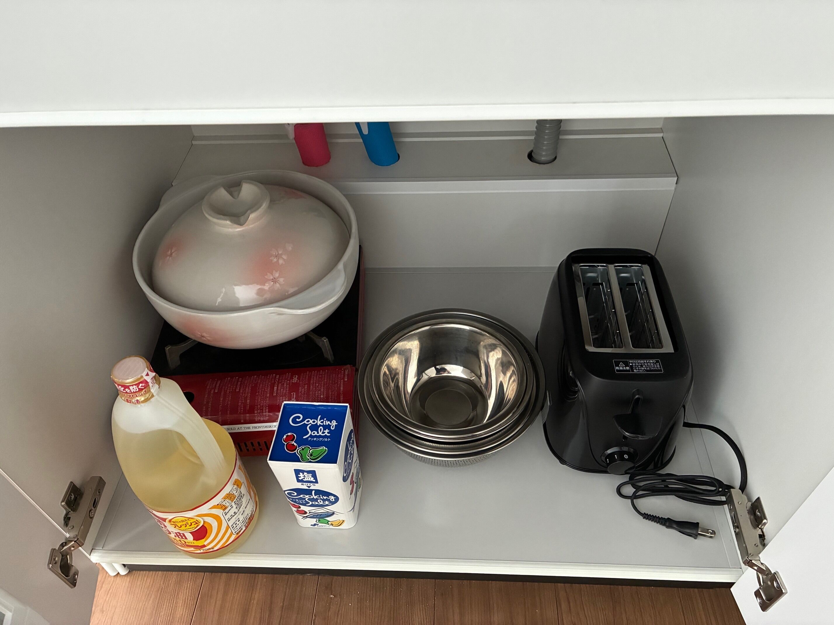 A kitchen counter with a pot, a box of cooking salt, a bottle of soy sauce, a toaster, and a metal bowl.