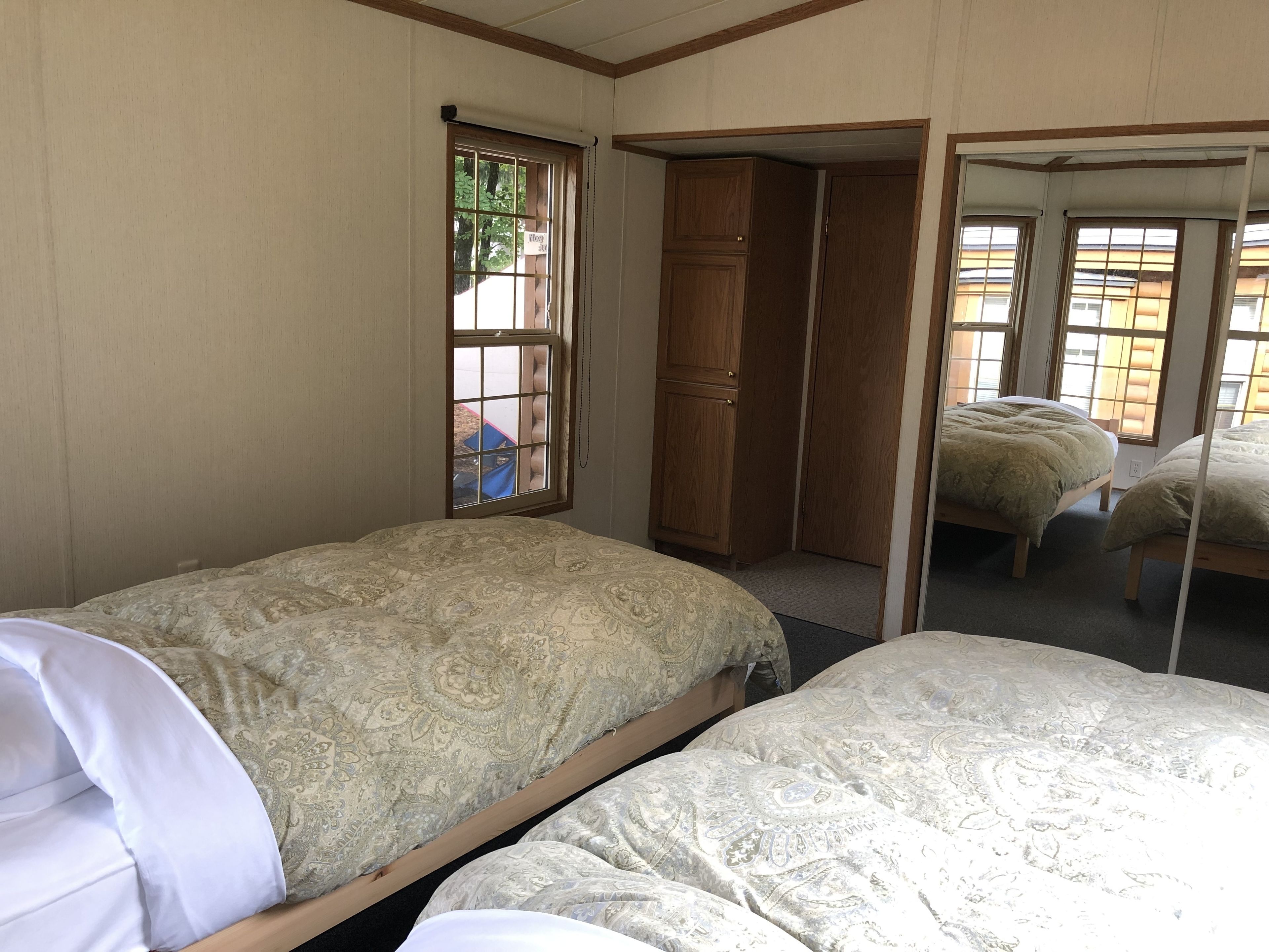 Een slaapkamer met twee eenpersoonsbedden, een houten garderobe en een raam met uitzicht op groen.