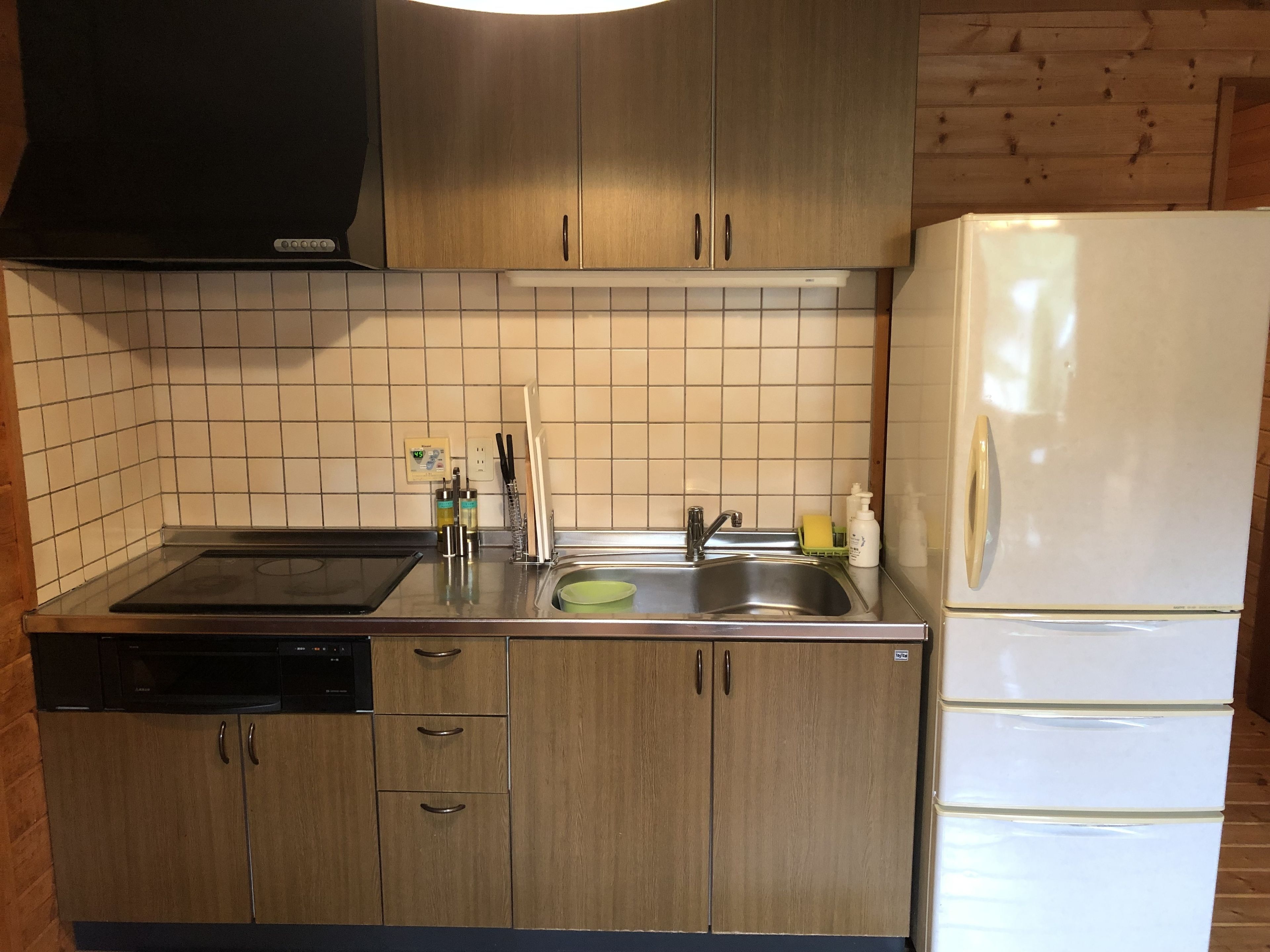 Cucina con mobili in legno, lavastoviglie integrata, piano cottura, lavello e frigorifero bianco.