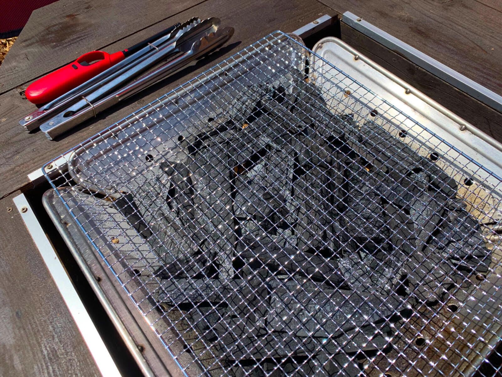Un barbecue au charbon de bois, avec une pince, posé sur une table en bois.