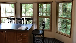 A corner room with a wooden desk, three chairs, and large windows offering a view of trees. - Hakuba Canadian Lodge (Hakuba)