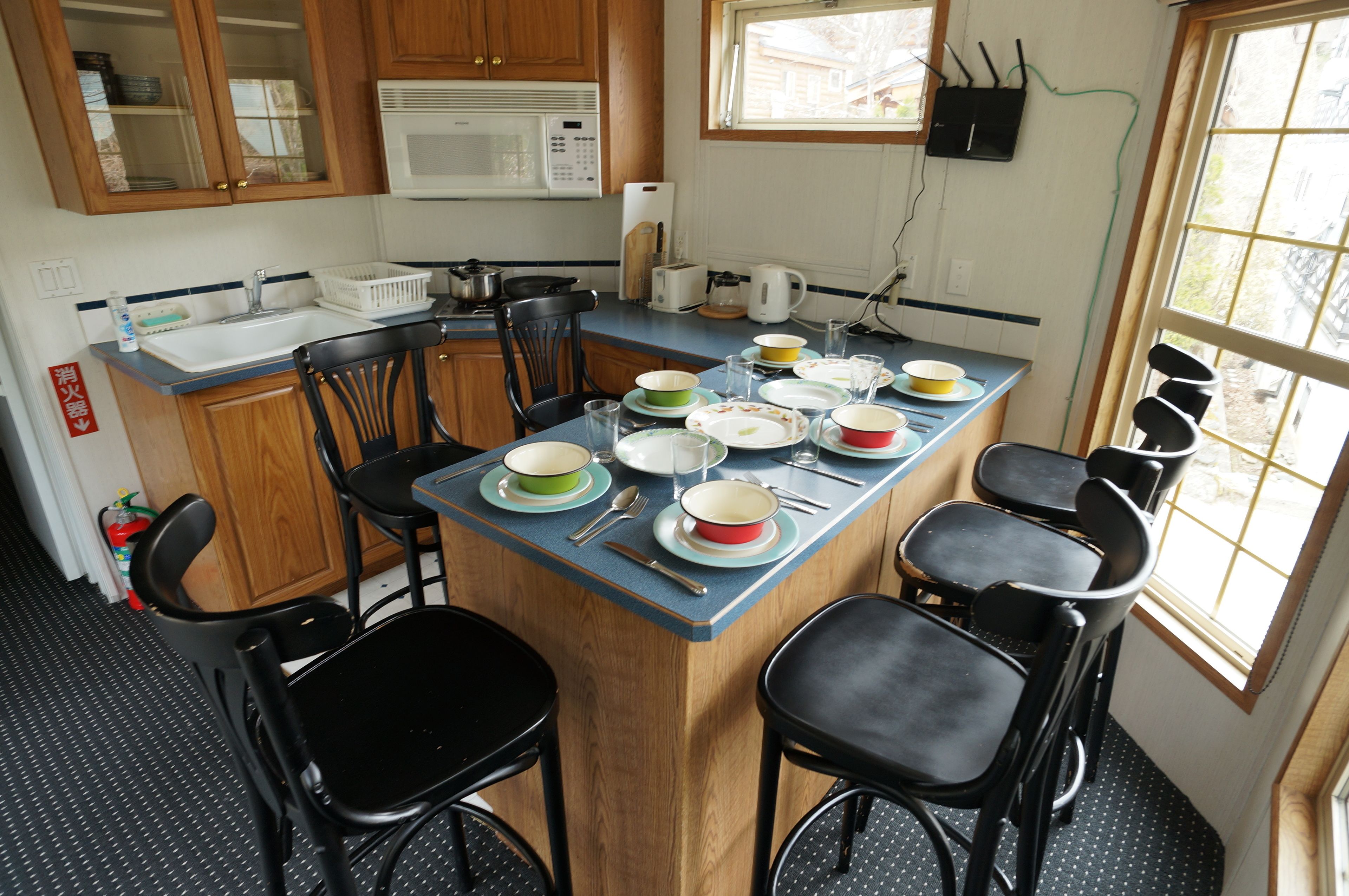 A compact kitchen with wooden cabinets, a microwave, a sink, and a dining area with chairs and a table set with dishes.