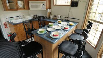 A compact kitchen with wooden cabinets, a microwave, a sink, and a dining area with chairs and a table set with dishes.