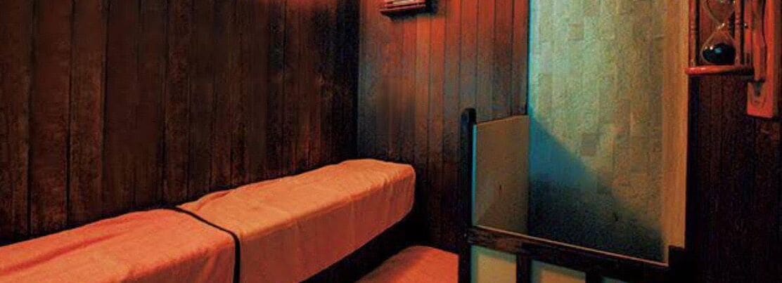 Une pièce aux murs en bois, un lit simple avec une couverture rouge et un miroir accroché au mur.