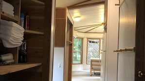 A narrow hallway with wooden shelving on one side, a bench in the center, and a door on the right. - Hakuba Canadian Lodge (Hakuba)