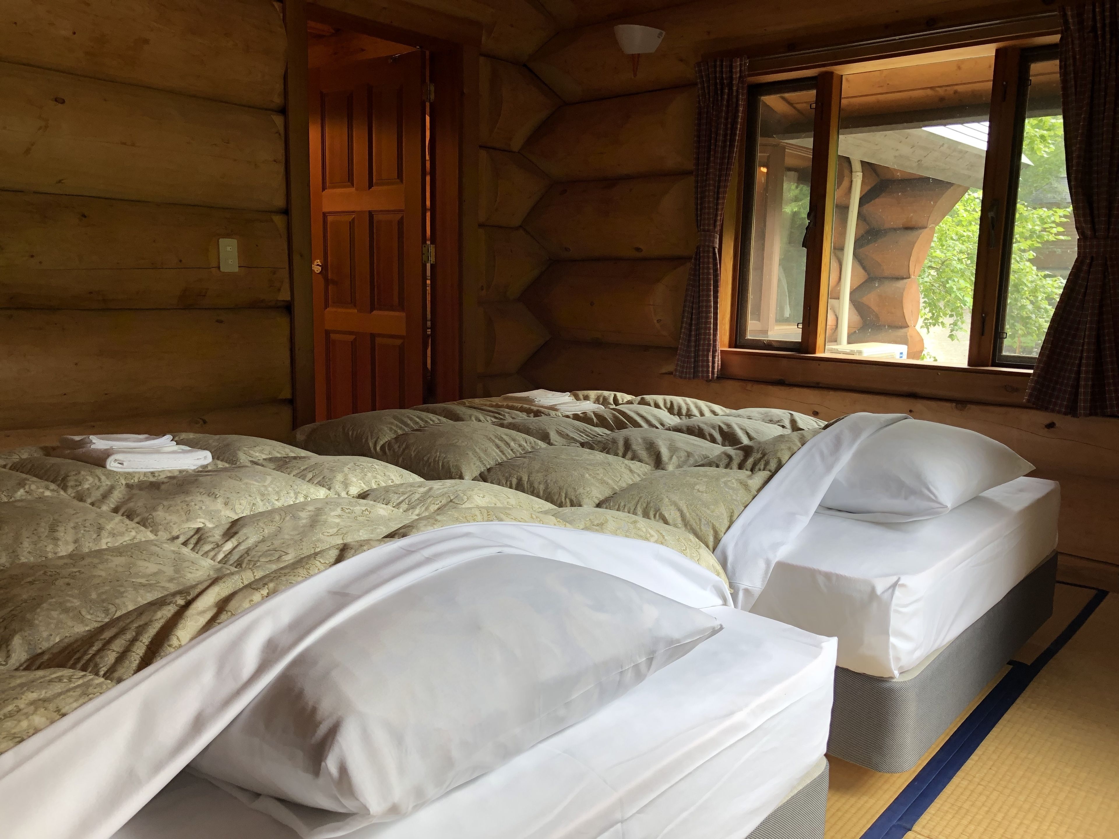 A cozy log cabin room with two beds, a wooden door, and a window with curtains.