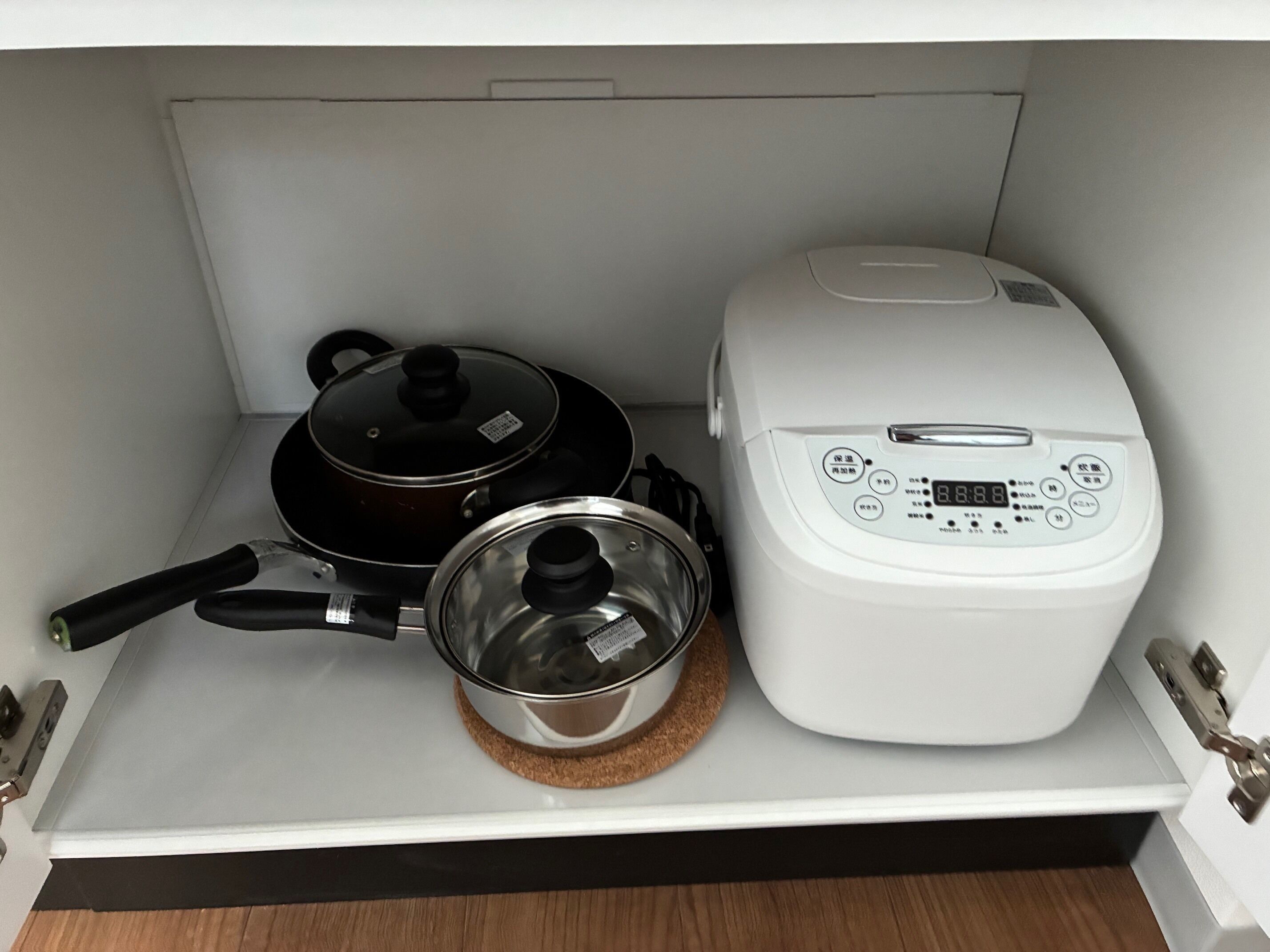 Une cuisine avec un cuiseur à riz et des casseroles rangées sur une étagère.