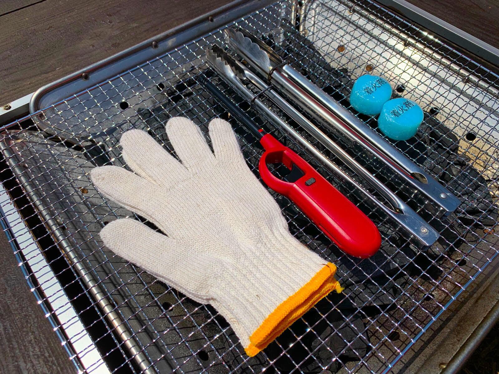 Un gril doté d’une grille en métal, un outil à manche rouge, un gant blanc et deux objets bleus.