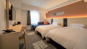 Ein Hotelzimmer mit zwei Betten, einem Schreibtisch, einem Stuhl, einem Fernseher und einem Fenster mit Vorhängen.