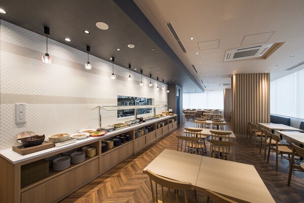 Un espace de restauration moderne doté d’un long comptoir, de plusieurs tables et offrant une vue sur la cuisine en arrière-plan.