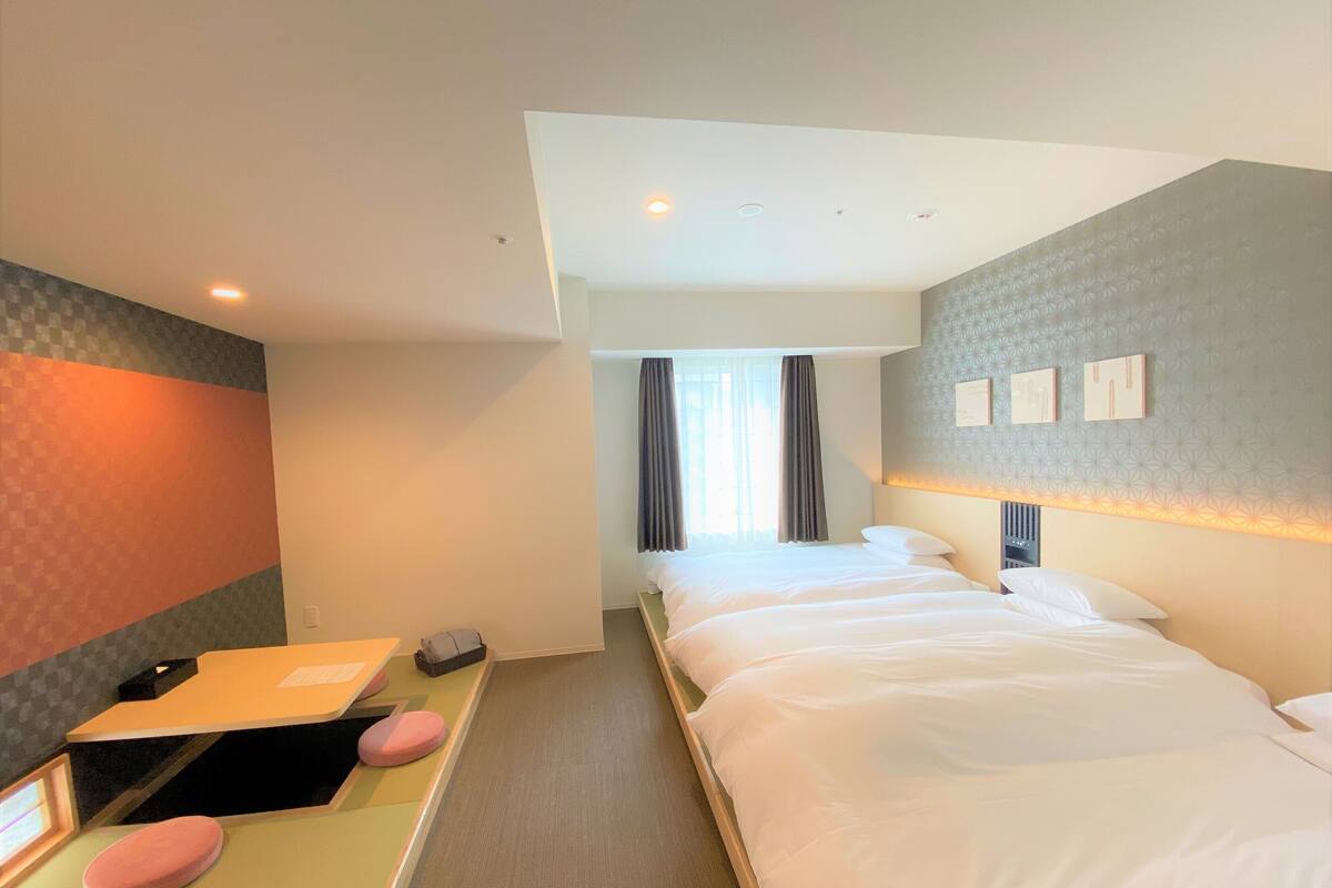 Ein Hotelzimmer mit Bett, Schreibtisch mit Stuhl, Spiegel und einem Fenster mit Vorhängen.