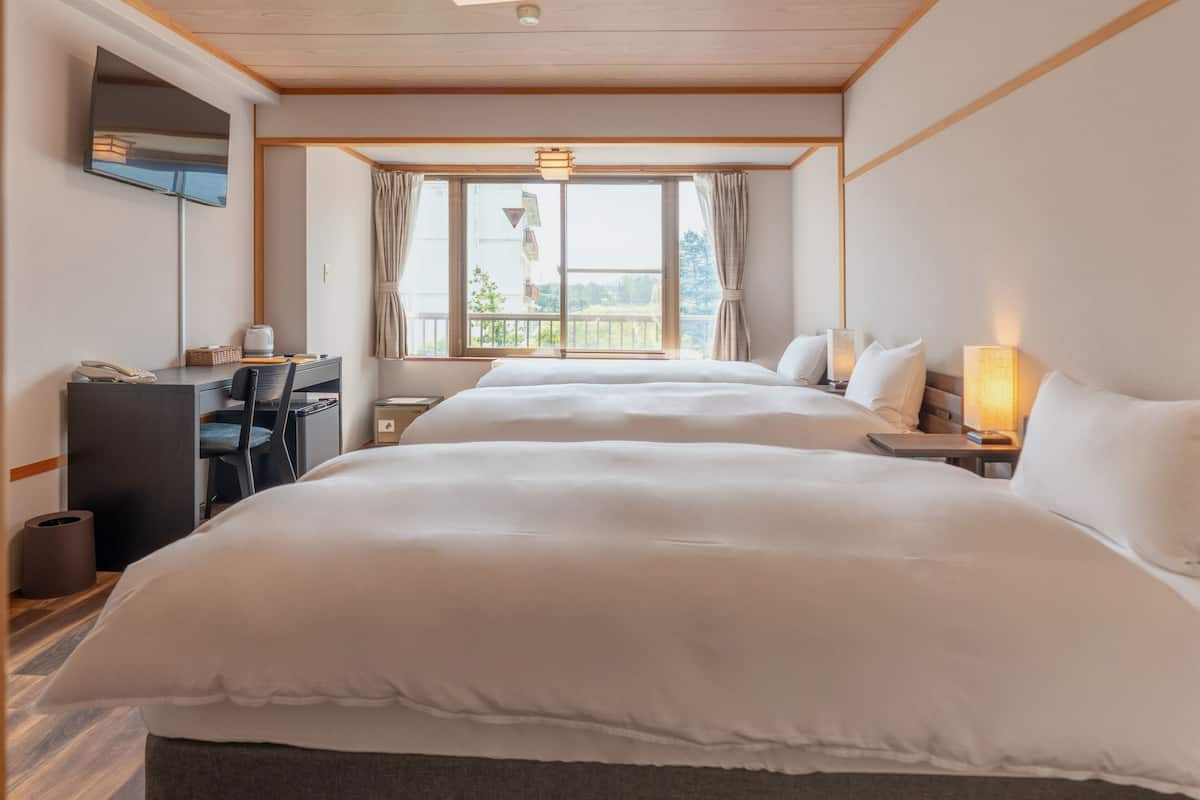 A hotel room with two beds, a desk, and a TV.