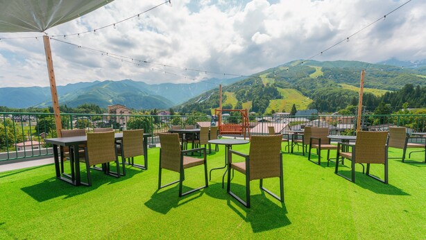 An outdoor seating area with tables and chairs, a view of mountains, and a green lawn. - SUMMIT VIEWS HAKUBA (Hakuba)