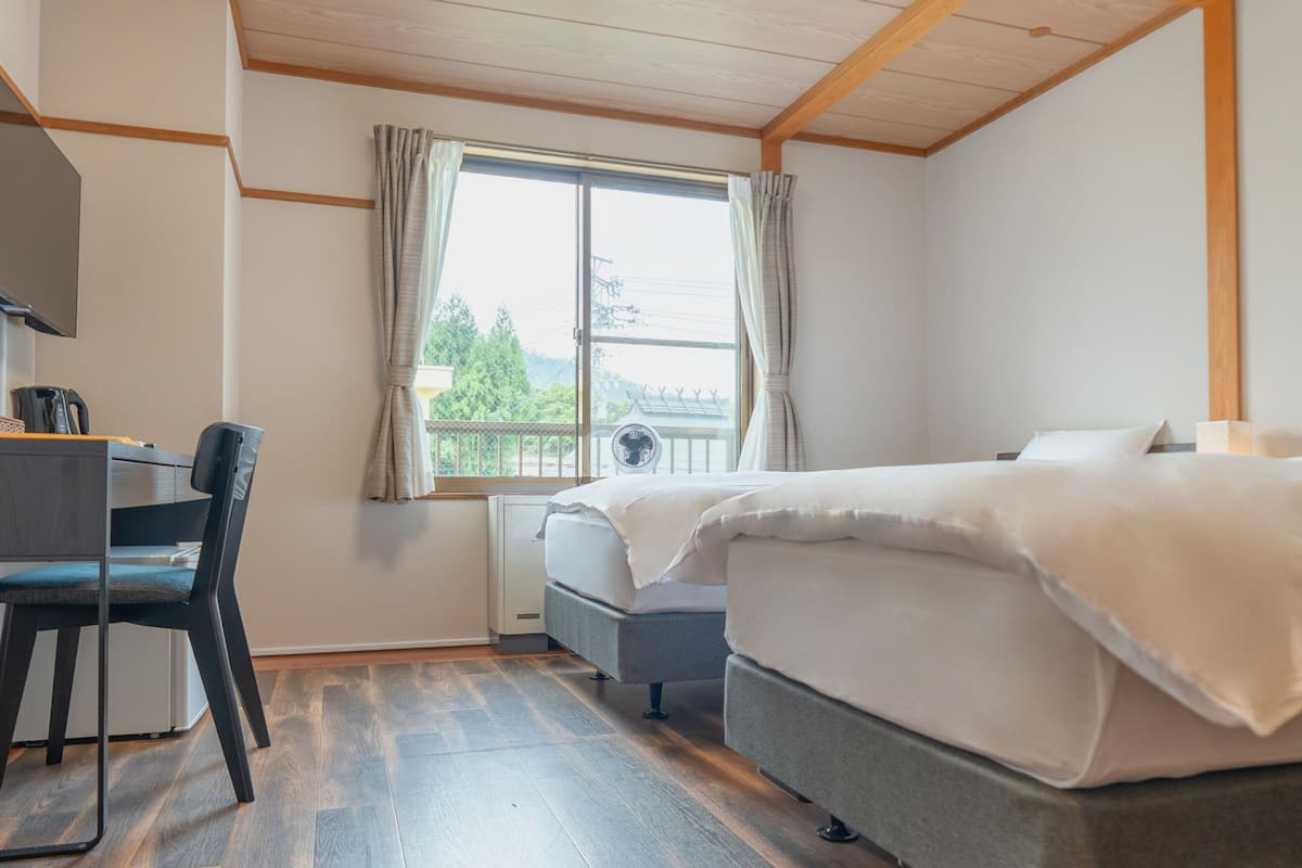 A bedroom with a bed, a desk with a chair, a window with curtains, and a radiator.