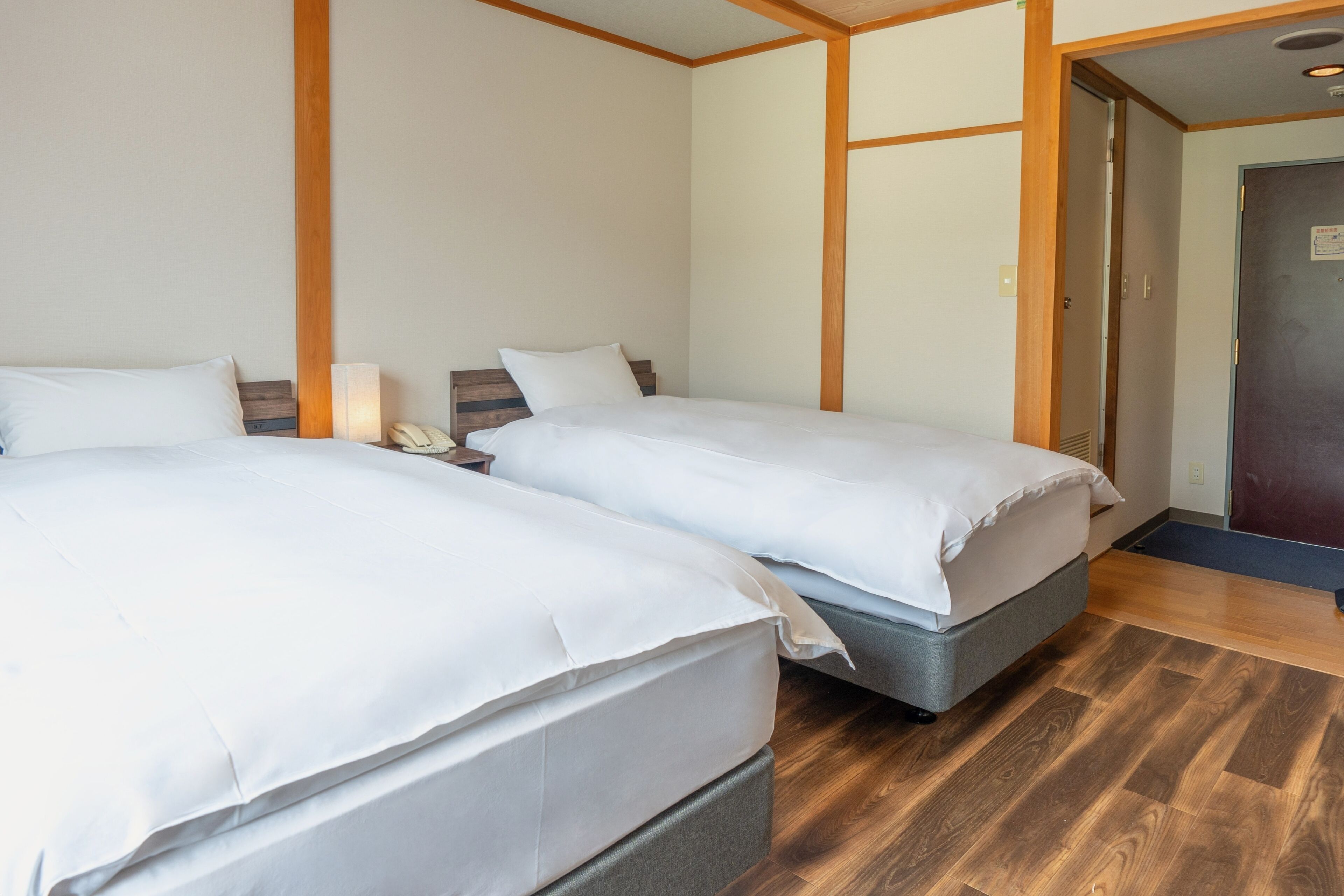 A hotel room with two beds, wooden paneling on the walls, and a wooden floor.