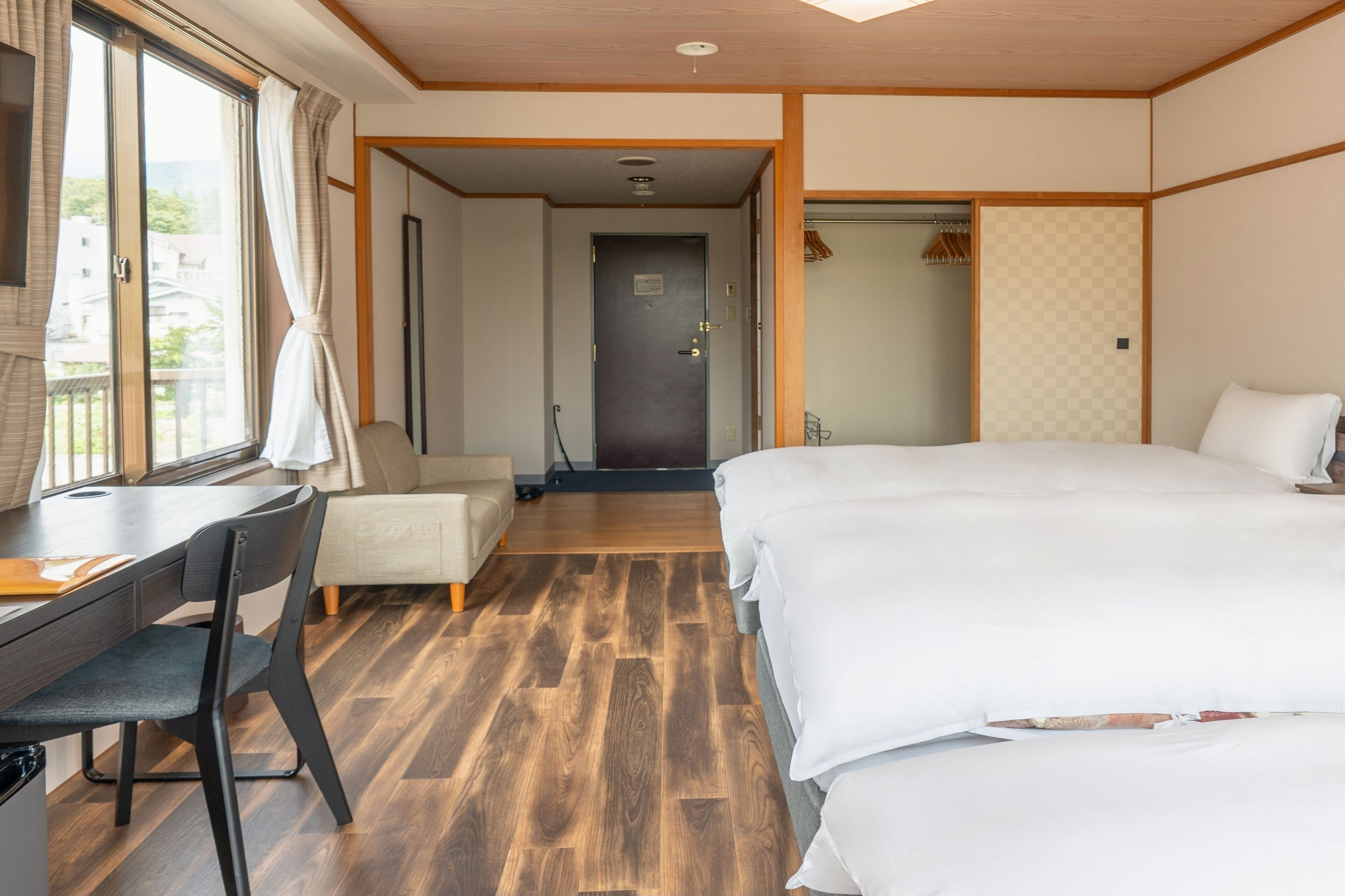 Habitación de hotel con suelo de madera, una cama, un escritorio con silla y una ventana con cortinas.