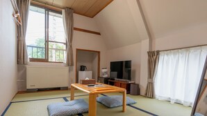 A traditional Japanese room with tatami flooring, a low wooden table, cushions, a television, and a window with curtains. - SUMMIT VIEWS HAKUBA (Hakuba)