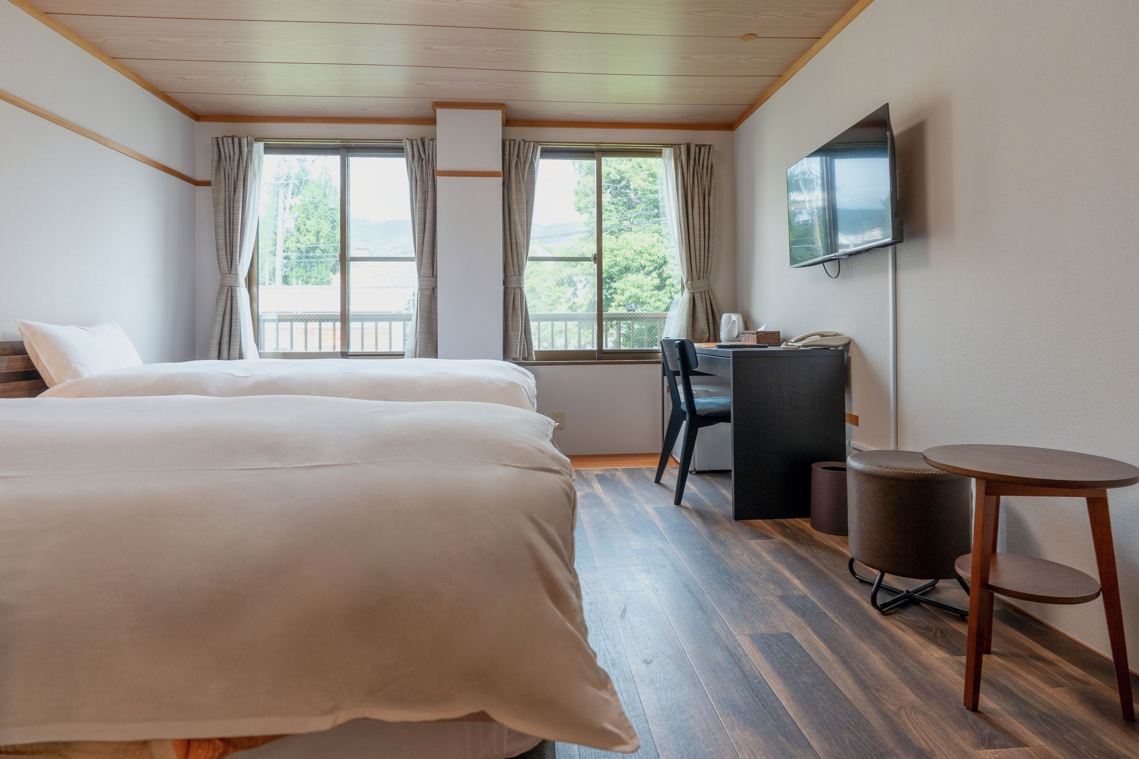 A hotel room with two beds, a desk, a chair, a small table, and a TV on the wall.