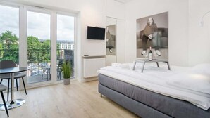 A modern hotel room with a large bed, a TV, a balcony with a table and chairs, and a view of the city. - Stylish Studio in the Center of Poznań | Balcony | Close to MTP (Poznan)