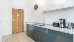 A modern kitchen with a wooden door, a sink, a coffee maker, and a kettle. - Stylish Studio in the Center of Poznań | Balcony | Close to MTP (Poznan)