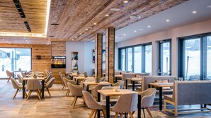 Un restaurante moderno con techo de madera y ventanas amplias. Mesas y sillas dispuestas para comer.