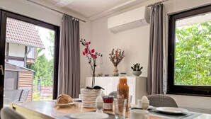 Un coin repas avec une table dressée pour deux personnes, une plante en pot et une vue sur la verdure à l’extérieur.