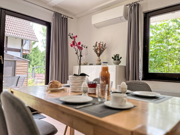 Comedor con una mesa preparada para dos, una planta en maceta y vistas al exterior.