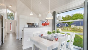 Een moderne keuken met witte kasten, een eethoek met een tafel voor vier personen en een uitzicht op huizen door grote ramen.