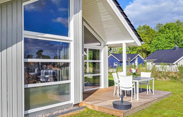 Una casa moderna con amplios ventanales, una terraza de madera y mobiliario exterior.