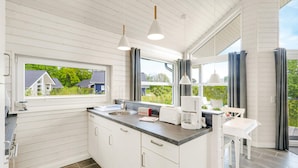 Een moderne keuken met witte kasten, een vast kookeiland, een koffiezetapparaat en uitzicht op huizen door grote ramen.