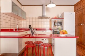 A kitchen with a red countertop, white cabinets, a stainless steel range hood, and a refrigerator.