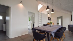 A modern dining area with a long table, black chairs, and pendant lighting. - Lovely home in Juelsminde with WiFi (Juelsminde)