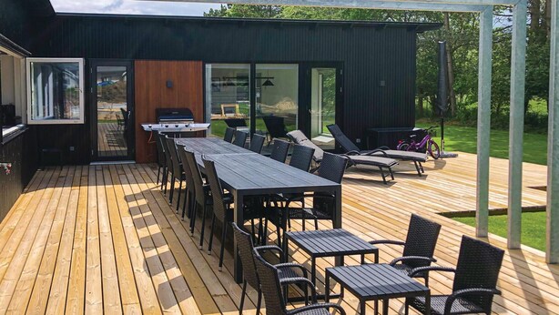 Eine moderne Terrassenanlage mit langem Tisch und Stühlen, einem Grill und einem Fahrrad.