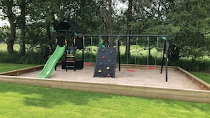 Ein Spielplatz mit Rutsche, Kletterwand und Schaukeln.