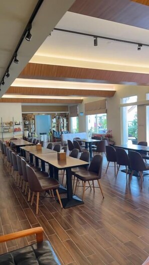 A spacious dining area with long tables and chairs, a kitchen in the background, and large windows allowing natural light. - Kinmen Yu Yuan (Jincheng)
