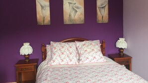 A bedroom with a purple wall, a wooden bed frame, floral bedding, and two bedside tables with lamps. - Apartment with terrace and garden (Saint-Jean-de-Luz)