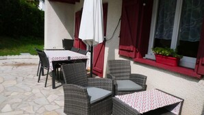 An outdoor patio with wicker furniture, a table, and chairs. - Apartment with terrace and garden (Saint-Jean-de-Luz)